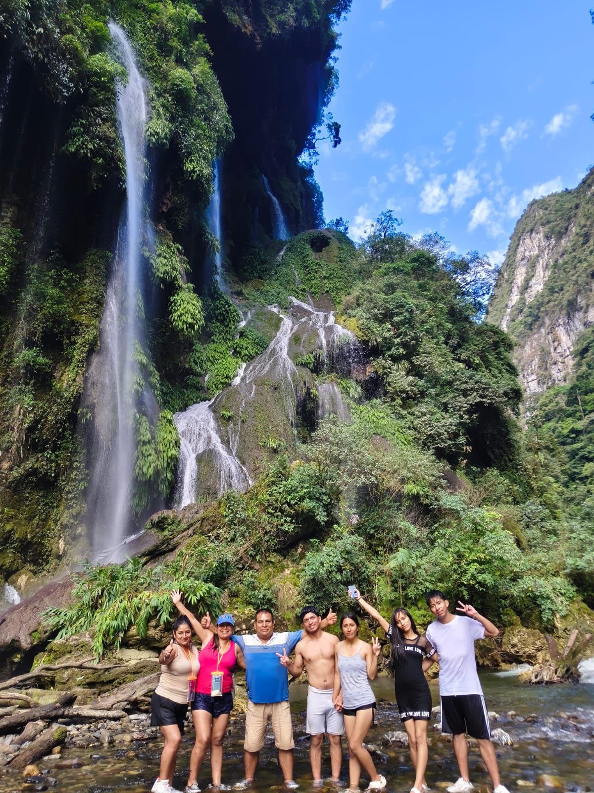 Grupo de visitantes en el río, con la catarata alta al fondo
